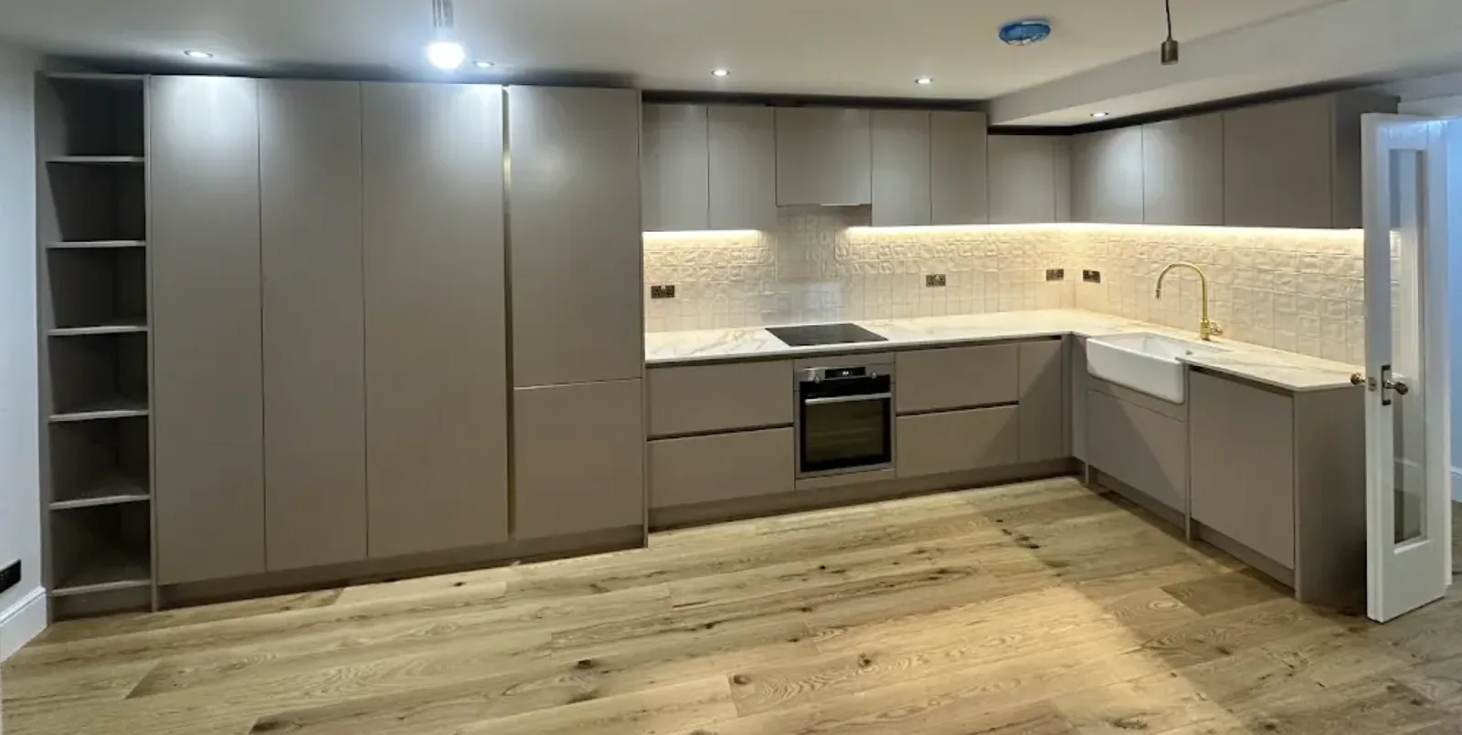 Grey handleless kitchen with marble effect worktops, a Belfast sink and brass tap