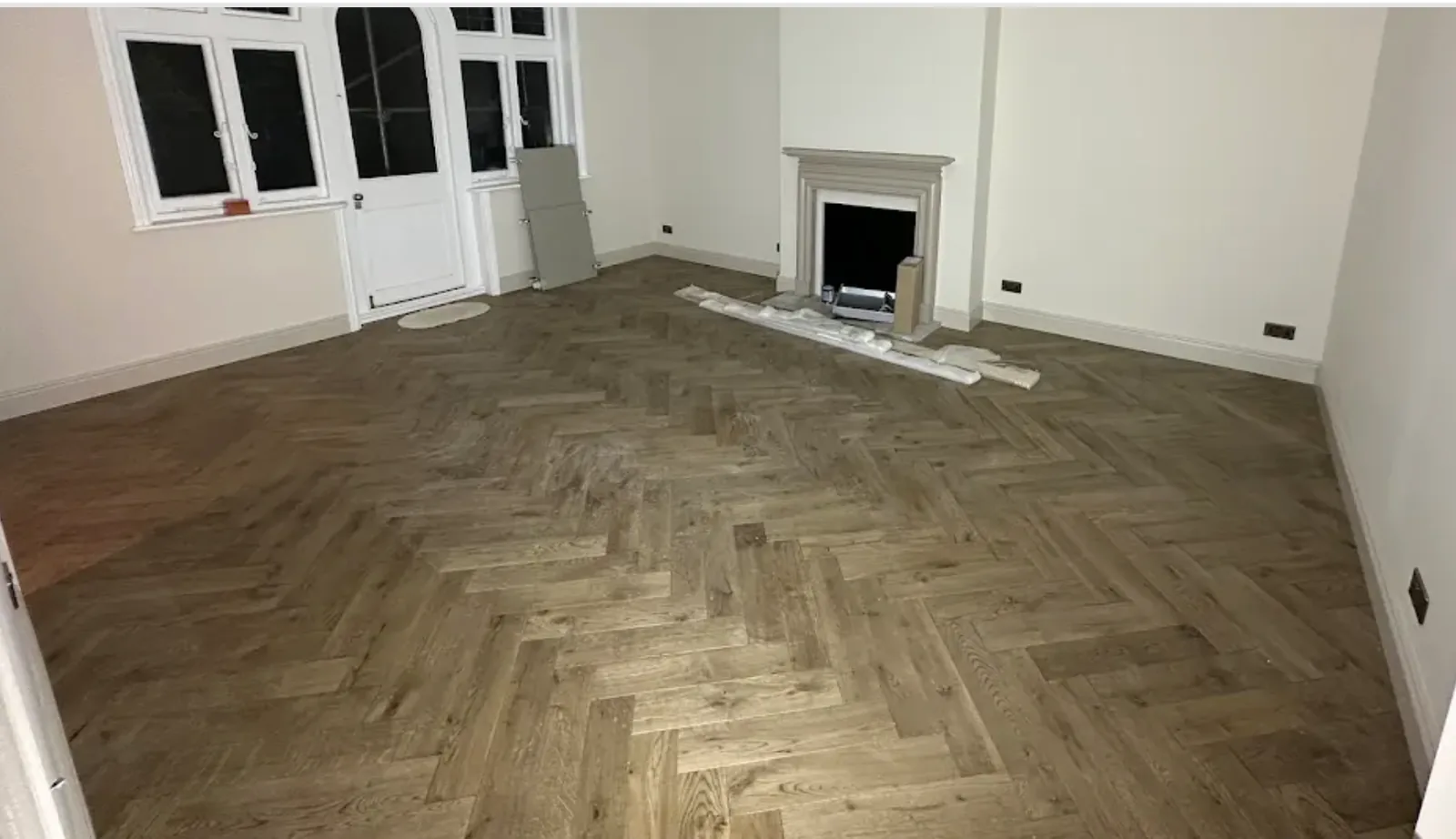 Period living room with a herringbone wood floor laid up to a stone fireplace and bay window