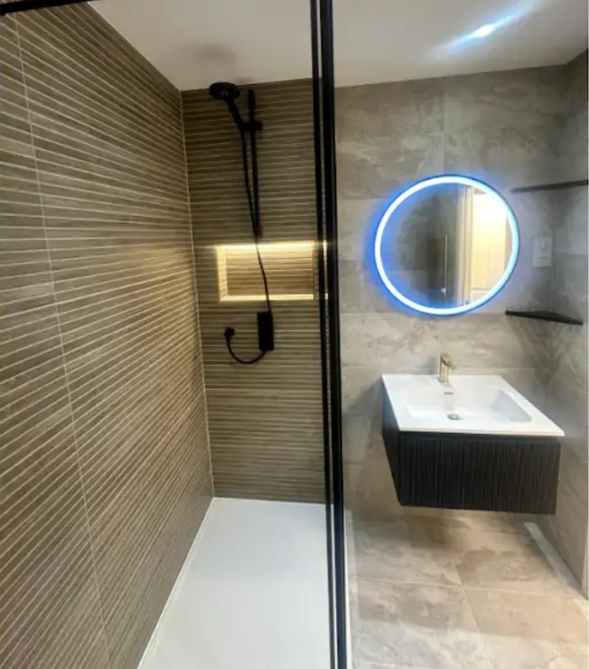 Walk-in wet room with stone effect tiling, a black framed screen and a round LED mirror